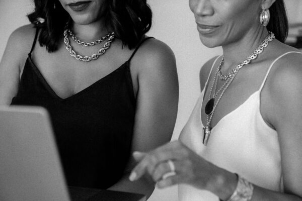 Two women are sitting at a desk with a laptop